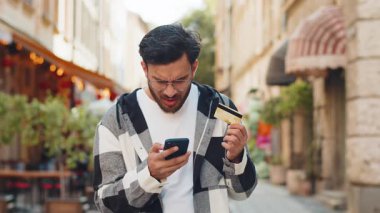 Hispanik bir adam internet üzerinden alışveriş yapmaya çalışırken akıllı telefonuyla kredi kartını bloke etmiş. Sokaktaki kızgın genç Arap turist, banka alım satımı reddediyor, ödeme dengesizliği yaşıyor.