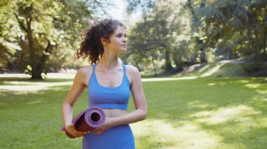 Sporcu fitness, spor yapmak için yoga minderiyle yürüyen genç bir kadın. Güzel yetişkin kız sabah parkta kardiyo antrenmanı yapıyor. Aktif sporcu kadın. Aerobik, kilo kaybı