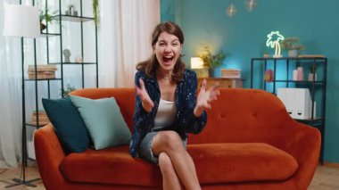 Kahverengi saçlı, mutlu bir kadının portresi TV izlerken evdeki oturma odasındaki kanepede oturup başarıyı kutluyor. Evde rahat giyinen heyecanlı bir yetişkin kız maçı kazanıyor..