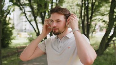 Kafkasyalı genç adam kablosuz modern kulaklıklar taktı. Koşucu, koşucu, spor koşucusu, koşucu, parkta koşan, müzik dinleyen, şarkı söyleyen, koşan, sağlıklı bir yaşam tarzı..