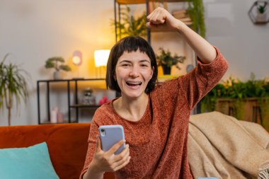 Şaşırdım, gülümseyen kadın akıllı telefon kazanan piyango kazanan kişi sınıftaki koltukta oturuyor. Heyecanlı Kafkasyalı kız dairede zafer kutlaması yapıyor yumruklarını sıkıyor. Mutlu bayan çevrimiçi oyun oynuyor