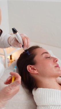 Alopecia. Kafkasyalı kız saç büyümesini hızlandırmak için dermapen ve vitamin enjeksiyonu ile hedeflenmiş kafa derisi terapisi görüyor. Kozmetik uzmanının mikronedling ve mezoterapi seanslarını yakından izlemesi