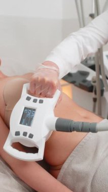 Genç bir kız kozmetolojist tarafından zayıf gösterme ve vücut şekillendirme için LPG cihazı kullanılarak karın vakum masajından geçiriliyor. Klinik prosedürü cilt bakımını, yağ bozulmasını, görünür şekil düzeltmesini teşvik eder.