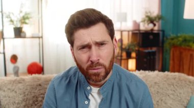 Evdeki genç adam kanepede oturuyor, kameraya şüpheyle bakıyor, gördüklerinden şüphe ediyor. Kafkasyalı adam şüpheci, şüpheci, kuşkucu, beklenmeyen bilgilerden şüphe duyan birine benziyor.