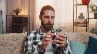 Genç adam evde oturmuş, hızlı bir şekilde telefondaki metni giriyor ve çevrimiçi market yerinde mükemmel bir indirim istiyor. Kanepede oturan adam inanılmaz bir ifade takınıyor ve çok faydalı bir teklif sunuyor.