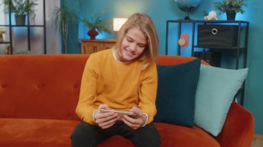 Akıllı telefondan oyun oynayan mutlu beyaz çocuk neşe ve heyecan yaşıyor. Çocuk oyunu kazanır, evdeki kanepede mutlu bir şekilde zıplar, 