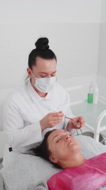 Enzim terapisi. Güzellik uzmanı orta yaşlı bir kadının alnına fırçayla nemlendirici krem maske takıyor. Kız cilt bakımı spa prosedürü. Yüz kozmetolojisi tedavisi. Dikey çekim