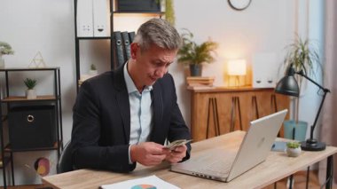 Zavallı Kafkasyalı genç iş adamı dolar sayarak para yetersizliği yaşıyor. Finansal kriz. İflas. Yoksulluk ve yoksulluk. Bilgisayarlı erkek ofis masasında oturuyor..