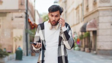 Sinirli, stresli Hintli genç adam, iki cep telefonuyla bağırarak konuşuyor. Sohbet ediyor, kavga ediyor, şikayet ediyor, sorunları dışarıda çözüyor. Şehir sokağındaki adam..