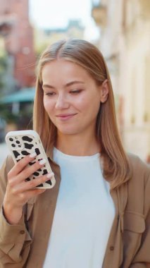 Akıllı telefon kullanarak mesajlar yazan güzel bir genç kadın. İnternetteki sosyal medya uygulamalarına bakarak dışarıda sohbet ediyor. Şehir caddesinde beyaz bir genç kız. Yaşam Tarzları