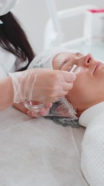 Güzellik uzmanı antioksidan gençleştirme uyguluyor. Kadının yüzüne asit serumu döküyor. Yaşlanma önleyici tedavi prosedürü kırışıklıkları ortadan kaldırıyor, siyah halkalar torbaları tansiyon eksikliği çekiyor..