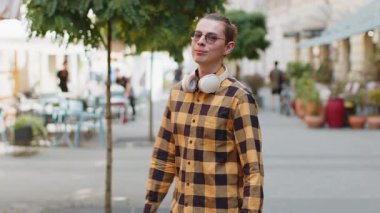 Mutlu bir adamın portresi arkasını döner ve arkasını döner. Dost canlısı, mutlu bir ifade. Kameraya bakar, kulaklıkları boynuna takar. Şehir sokağındaki adam.