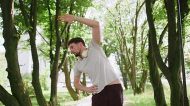 Spor kıyafetleri içinde atletik beyaz bir adam vücut geriyor ve egzersiz yapmadan önce ısınıyor. Parkta koşan yakışıklı bir genç. Spor sağlık, spor rutini, egzersiz. Kuvvet ve motivasyon.