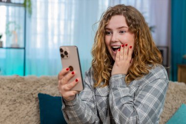 Evde cep telefonunu kaydıran genç bir kadın, haber, indirim ya da Kafkasyalı bayanı temsil eden kazanan sonuç için heyecanlanıyor. Kanepedeki kızıl saçlı kız haykırıyor. Şaşırmış, sevinçli bir kutlama reaksiyonu gösteriyor.