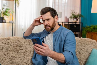 Evde orta yaşlı bir adam akıllı telefondan mesaj atarken gergin ve hayal kırıklığına uğramış hissediyor. Gergin, beyaz bir adam koltukta oturmuş, endişeyle önemli bir mesaj bekliyor.