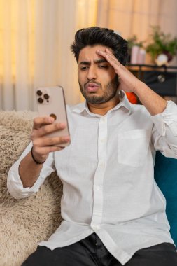 Evde akıllı telefon tutan Hintli bir adam, elleri başının üstünde, kötü haberlere tepki veriyor, endişeli ve üzgün hissediyor. Arap adam olumsuz mesaj okuyor, stresli, hayal kırıklığına uğramış, beklenmedik bir durum yaşıyor.