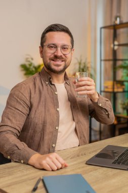 Ofis odasında dizüstü bilgisayarla çalışırken masa başında oturmuş su içen Kafkasyalı bir iş adamı. Genç erkek serbest çalışan adam bilgisayar ekranı internette geziniyor..