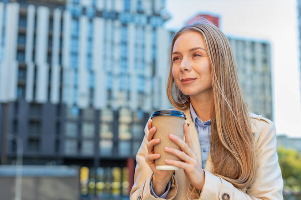 Happy mature businesswoman enjoying morning coffee hot drink and smiling outdoors. Relaxing, taking a break. Girl drinking coffee to go walking on downtown urban city street. Town lifestyles outside.