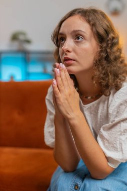 Korkunç haberlerle şoke olmuş, üzgün genç bir kadın, avuç içlerini birleştirip yardım diliyor, stresli olduğunu düşünüyor. Hayattaki sorunlar yüzünden umutsuz görünüyor. Dua ediyor, yardım istiyor. Dikey.