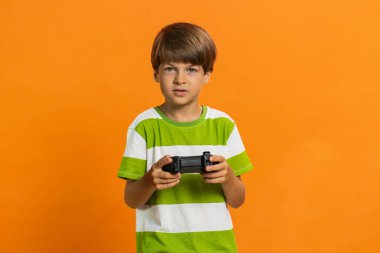 Oyun konsolu oyunu oynayan, oyun konsolu kullanan küçük çocuk hafta sonları online oyun kazanmanın keyfini çıkarıyor. Turuncu arka planda izole edilmiş küçük çocuklar