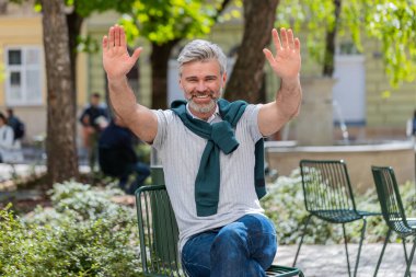 Neşeli olgun turist, kameraya gülümseyen, el sallayan, el sallayan davetkar merhaba, merhaba, merhaba, güle güle, misafirperver bir yüz ifadesiyle hoş geldiniz. Şehir merkezindeki adam..