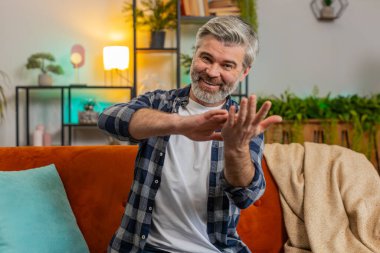 Kendine güveni tam, olgun bir adam harcıyor ya da el hareketleriyle etrafa para saçıyor. Büyük kar getiren vücut dili hakkında daha fazla bahşiş alıyor. Mutlu son sınıf Kafkasyalı orta yaşlı adam dairede koltukta oturuyor.