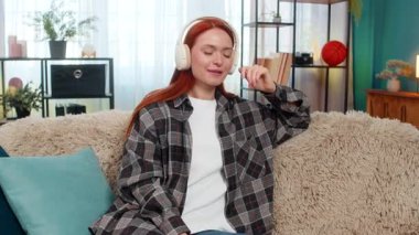 Evde kablosuz kulaklık takan, gözleri kapalı, favori müzik dinleyen genç bir kadın. Kanepede oturan beyaz saçlı kız sakin duygusal dengesiyle huzurlu bir ses anının tadını çıkarıyor..