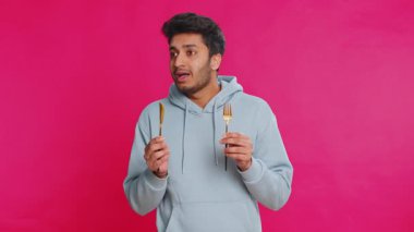 Çatal ve bıçak tutan aç Hintli adam lezzetli bir yemek bekliyor, heyecandan dudaklarını yalıyor. Açlıktan kıvranan Arap adam, pembe arka planda sabırsız bir ifadeyle yemek istiyor.