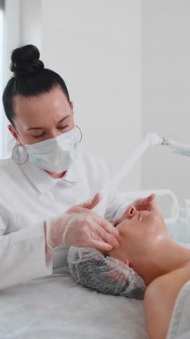 Güzellik uzmanı, genç yetişkin kadın yüzüne nemlendirici tıbbi kimyasallar soyarak krem fırçalama maskesi uyguluyor. Dişi cilt bakımı prosedürü. Yüz kozmetolojisi cilt yenilenmesi. Dikey