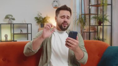 Kafkasyalı bir adamın oturma odasındaki kanepede oturarak akıllı telefon kullanmasından rahatsız oldum. Kafasına dokunan sıradan giysili genç adam aniden piyango ya da kötü haberlere şaşırır..