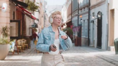 Kablosuz kulaklıklı mutlu, gevşemiş genç sarışın kız en sevilen disko rock n roll müziğini dinliyor, açık havada dans ediyor. Beyaz kadın turist şehir caddesinde yürüyor.