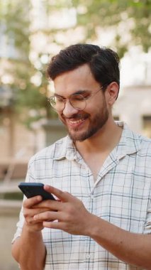 Hintli genç adam sosyal medya uygulamasında akıllı telefon kullanarak kısa mesajlar yazıyor, internette sörf yapıyor, dinleniyor, dışarıda mola veriyor. Şehir caddesinde duran İspanyol adam. Dikey