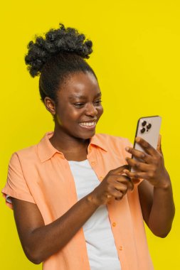 Afro-Amerikalı kadınlar akıllı telefonlara sahipler, sosyal medyayı meşgul tutuyorlar, ara sıra mesajlardan hoşlanıyorlar. Sarı arka planda izole edilmiş siyah kız içeriğe ve olumlu tepkilere ilgi gösteriyor