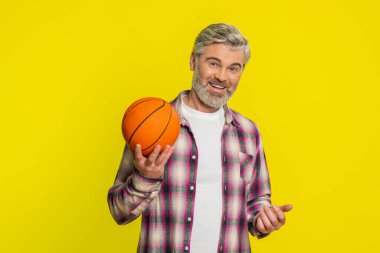 Olgun bir erkek, basketbolu ustalıkla elinde zıplatır, oyun oynar, kendine güvenini gösterir, kontrollü davranır. Sarı arka plandaki orta yaşlı adam atletik inceliği, parmak ucunda dönen topu gösteriyor.