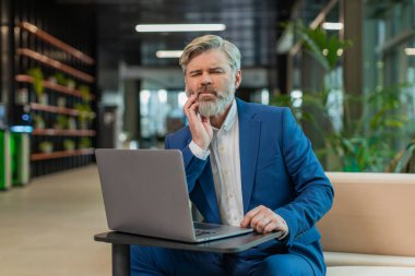 Ofis lobisindeki beyaz iş adamı dizüstü bilgisayarla çalışıyor ve diş ağrısının elinle yanağa değdiğini hissediyor diş hastalığından dolayı acı veren bir ifade. Pulpitis, sakız hastalığı, diş hastalıkları konsepti.