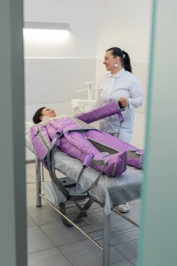 Kozmetik uzmanı hastaların ellerine takım elbise giyip pressooterapi uyguluyor. Selülitlerle mücadelede kullanılan donanım kozmetolojisi tekniği. Sıkıştırılmış hava desteği ile lenfatik sistemi etkiler