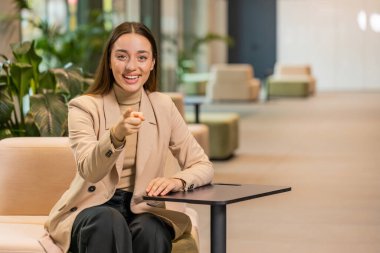 Seni seçiyorum. Kafkasyalı genç iş kadını yazılım geliştirici kamerayı işaret ederek, mutlu bir ifadeyle bakarak, işe alma seçimini yapıyor. Ofis lobisinde serbest çalışan kız..