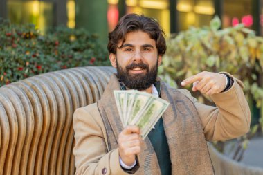 Şehir merkezindeki caddede elinde dolar banknotları tutan başarılı genç Hintli adam. Mutlu yetişkin Hindu adam çevrimiçi piyango oyunu kazanıyor. Bütçeyi hesaplamak için nakit kredi teklif ediyor.