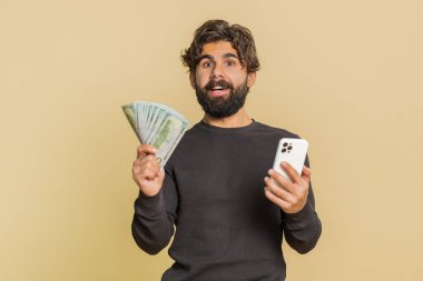 Lübnanlı genç adam akıllı telefonu samimi bir şekilde neşeyle kazanıyor, para dolar banknotları alıyor, piyango talihi, gelir maaşı alıyor. Stüdyo bej arka planda Hintli adam..