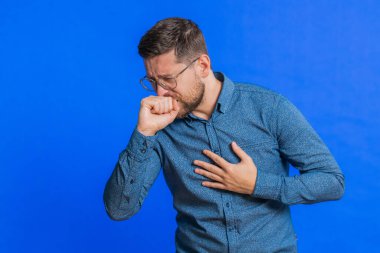 Sağlıksız, orta yaşlı, gözlüklü, öksüren, elinde grip belirtileri olan hasta, alerji, ateş ya da viral enfeksiyon olan orta yaşlı bir adam. Hasta adam mavi arka planda izole edilmiş.