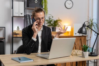 Mutlu Kafkas tarzı genç iş adamı müşteriyle telefon akıllı telefonuyla iletişim kuruyor, ofis masasında dizüstü bilgisayar ağı üzerinde çalışıyor. Takım elbiseli adam internetteki uzak mesafe işini temsil ediyor..