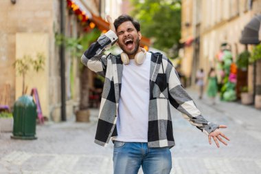 Hintli genç adam bağırıyor stres yüzünden bağırıyor korku, umutsuzluk panik, sürpriz şok, öfke belirtileri hissediyor. Şehir caddesinde duran sinirli İspanyol adam..