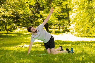 Formda, esnek bir adam parkta spor minderinde yoga yapıyor. Kollarını kaldır. Genç erkek, dışarıda egzersiz yapmaktan hoşlanıyor. Aktif sporcu motivasyonu. Kararlı sporcu sağlıklı yaşam tarzı.