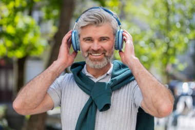 Kablosuz kulaklıklar takıp açık havada akıllı telefon uygulamasında en sevilen enerjik müziği dinleyen olgun, beyaz bir adam. Sakallı bir turist, Sunshine City caddesinin yanından geçiyor. Yaşam Tarzları