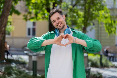 Ben de seni seviyorum. Beyaz adam aşkın sembolünü yapar, kameraya kalp işaretini gösterir, romantik duyguları ifade eder, samimi olumlu duyguları ifade eder. Sadaka, minnettarlık, bağış. Şehir caddesinde açık hava