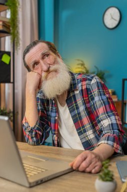 Düşünceli, düşünceli, üst düzey bir adam dizüstü bilgisayarda çalışıyor. Başka tarafa bakıyor. Ofisteki sorunu çözmeyi düşünüyor. Büyükbaba ilham arayışında. Karar vermede fikir yoksunluğu çekiyor. Dikey