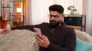 Hintli adam eski kız arkadaşının sosyal medya profiline üzgün gözlerle ve derin bir iç çekişle bakıyor. Kanepedeki Arap adam akıllı telefonu yavaşça kenara koyuyor, nostaljik, hayal kırıklığına uğramış ve duygusal olarak yorgun hissediyor.