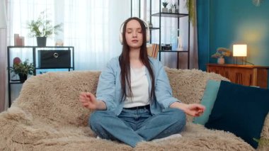 Genç ve güzel bir kadın evde sakin sakin gözleriyle rahatlıyor, sessizce nefes alıyor kulaklıkla meditasyon müziği dinliyor. Kafkasyalı kız kanepede huzur içinde meditasyon yapıyor, sükuneti ve farkındalığı hissediyor..