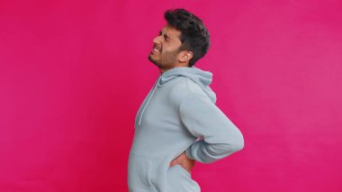 Sırt ağrısı çeken Hintli bir adam, masaj yapan yaralı bir yer alt omurga, dayanılmaz spazm yüzünden kaşlarını çatan yırtık kaslar ve tendonlar, böbrek taşları sinirleri sıkıyor. İçerideki pembe arka planda izole edilmiş Arap bir adam.