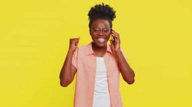Telefon, iyi haber, dedikodu. Afro-Amerikan genç bayanı mutlu bir şekilde akıllı telefondan keyifli bir sohbete daldı, arkadaşlarıyla konuşmaktan keyif alıyordu. İçerideki sarı arka planda izole edilmiş siyah kız.